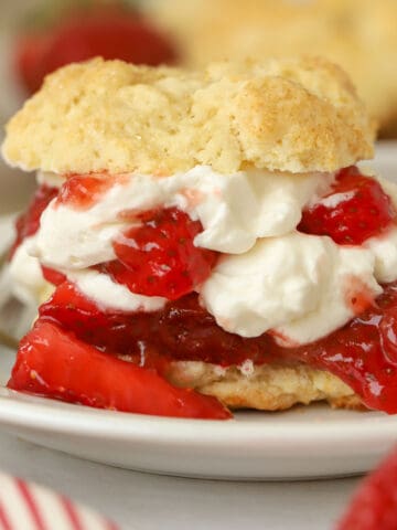 Layered strawberry shortcake on a white plate next to a fresh strawberry.