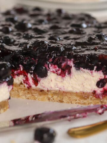 Blueberry dessert bars on parchment paper next to a gold fork.