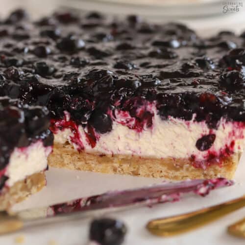 Blueberry dessert bars on parchment paper next to a gold fork.
