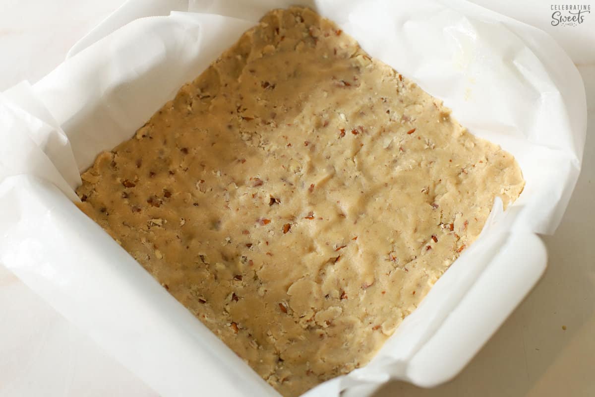 Unbaked pecan shortbread crust in a white square baking pan.
