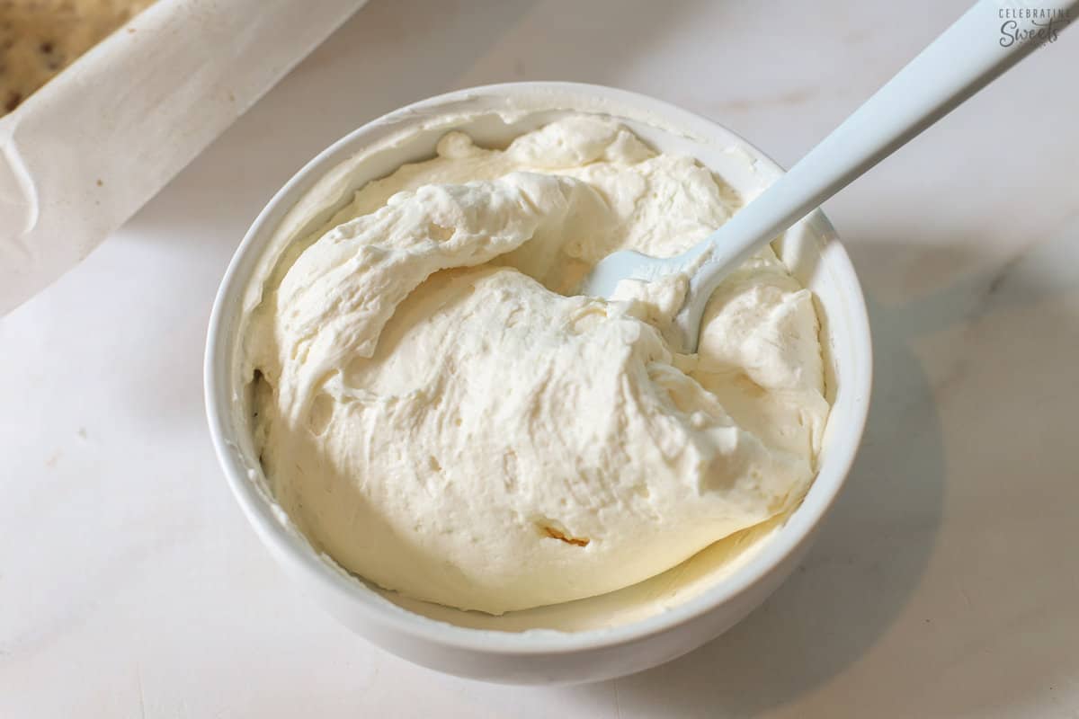 Cheesecake whipped cream in a white bowl with a rubber spatula.