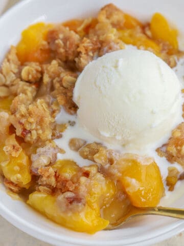 Peach crisp topped with vanilla ice cream in a white bowl.