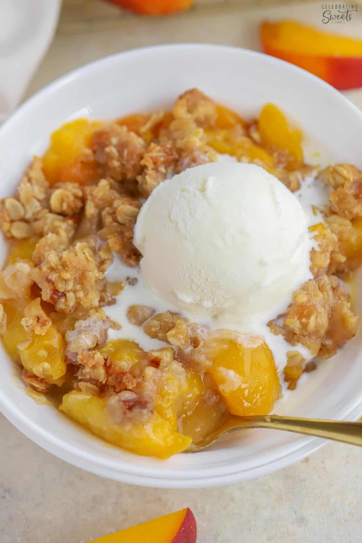 Peach crisp topped with vanilla ice cream in a white bowl.