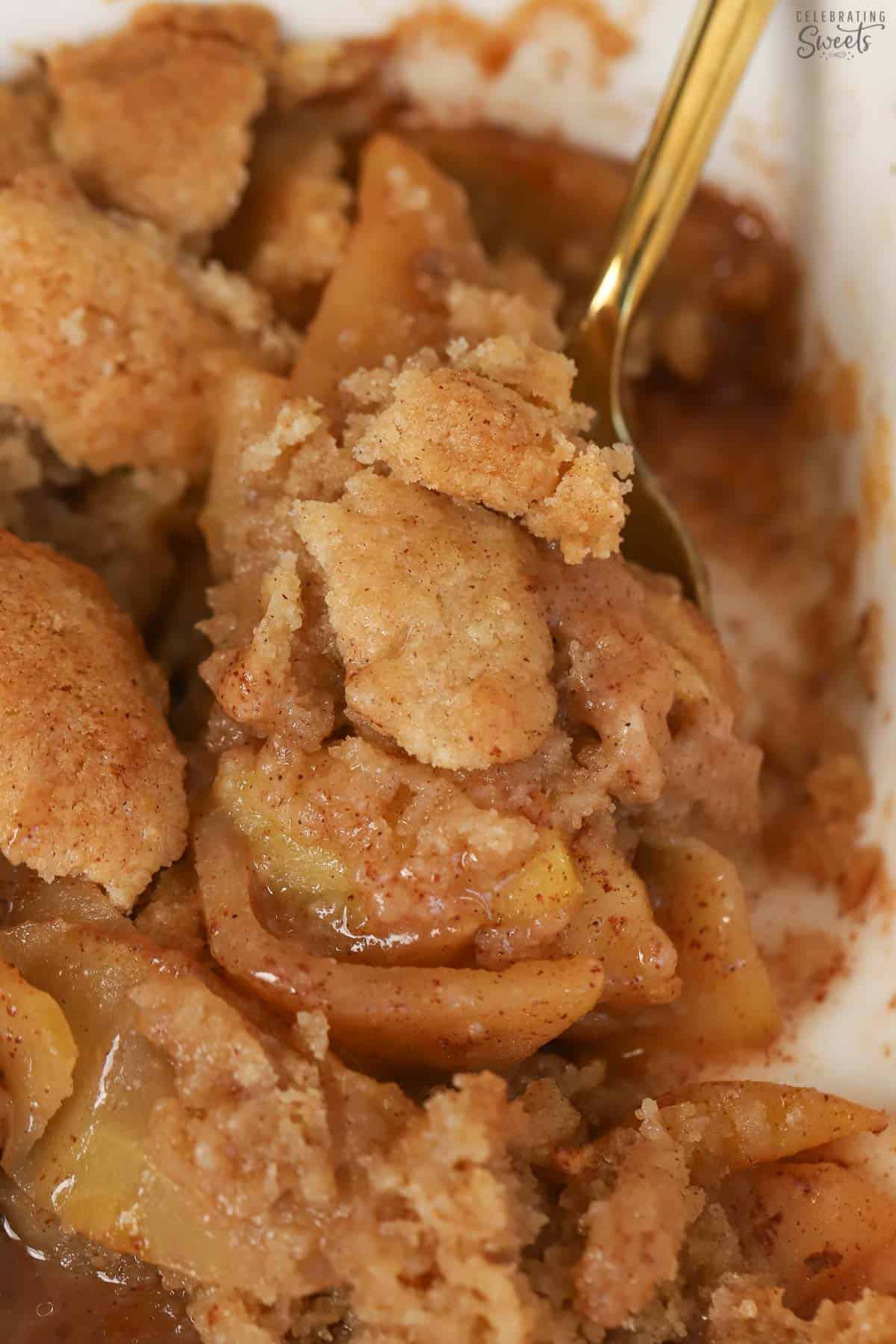 Apple cobbler in a white baking dish with a gold spoon.