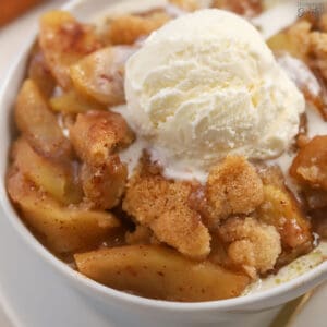 Apple cobbler in a white bowl topped with vanilla ice cream.