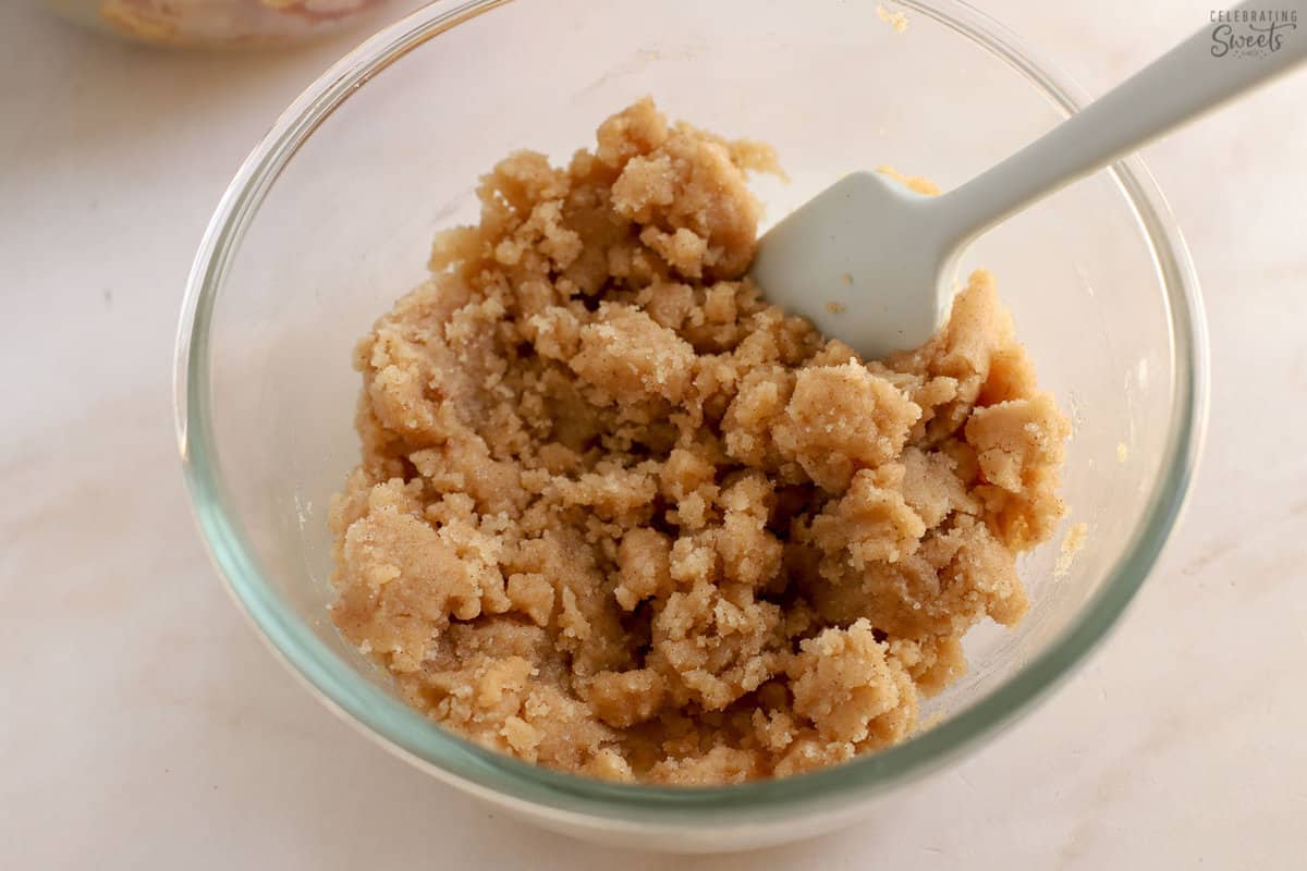 Apple cobbler topping in a glass bowl with a grey spatula.
