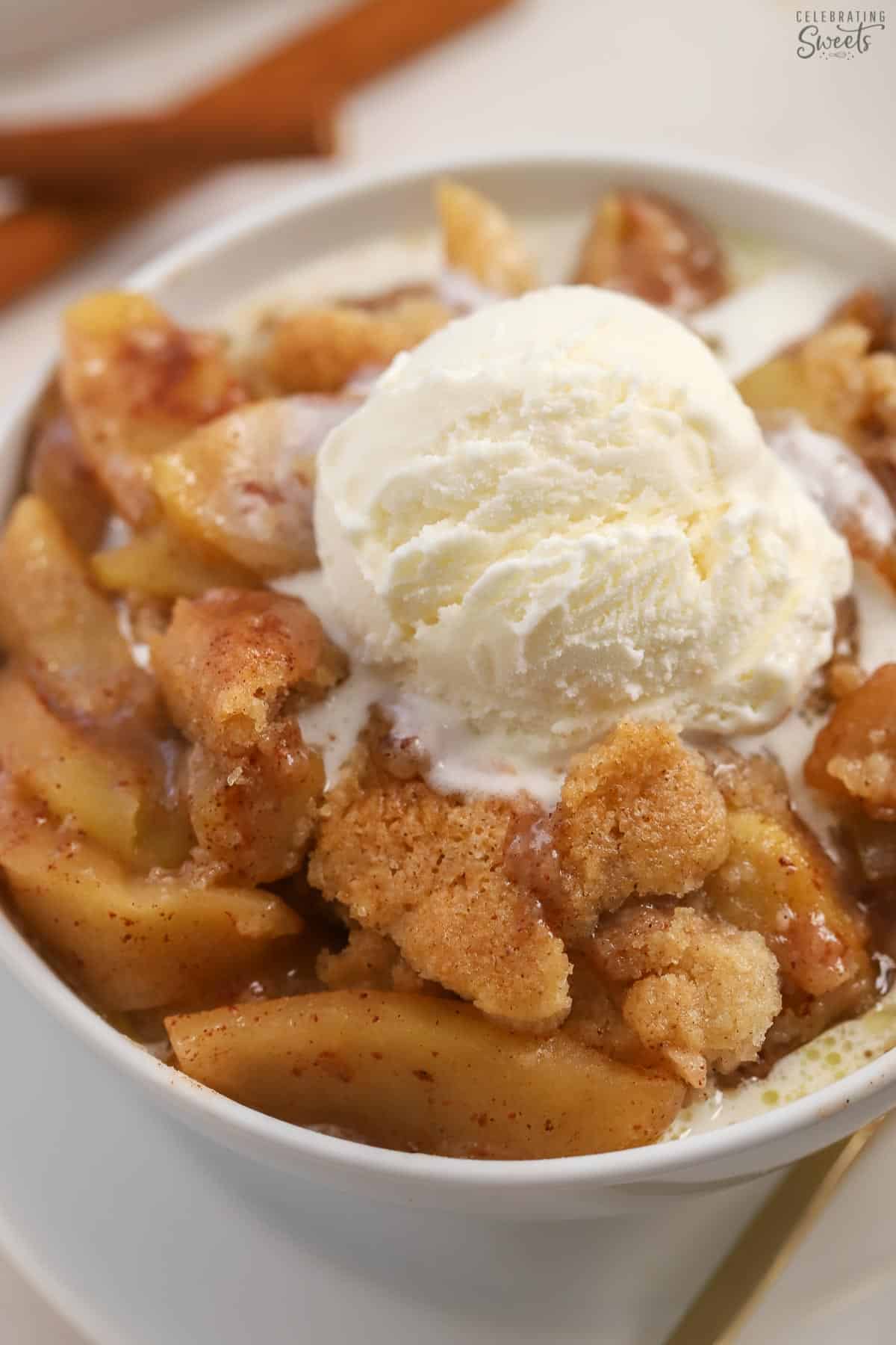 Apple cobbler in a white bowl with a scoop of vanilla ice cream on top.
