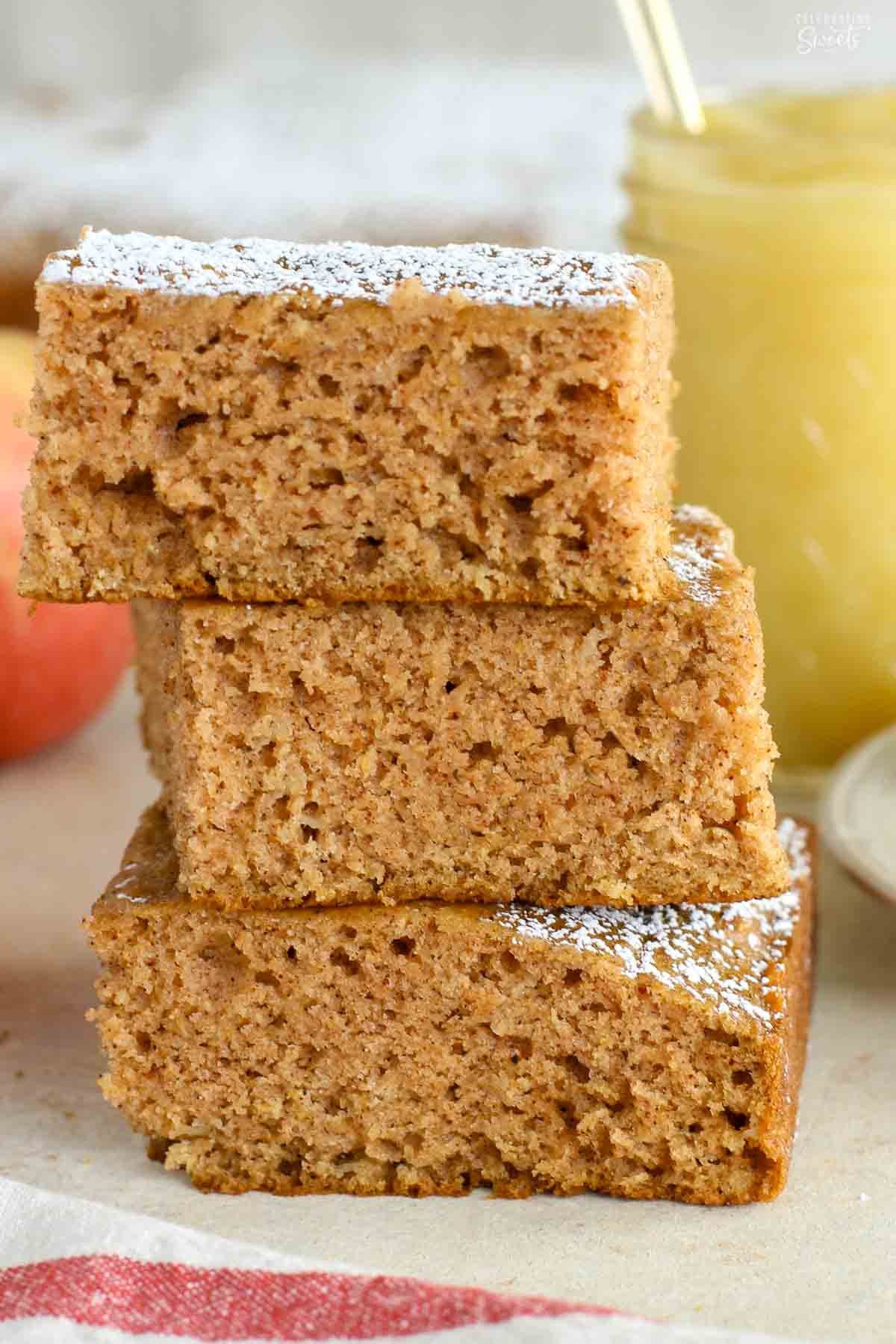 Three pieces of applesauce cake stacked on top of each other with a jar of applesauce in the background.
