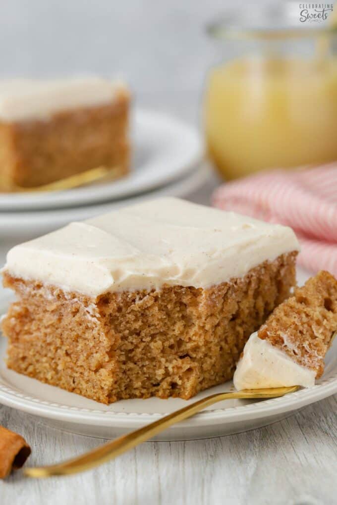 Slice of applesauce cake topped with cream cheese frosting on a small plate with a gold fork.