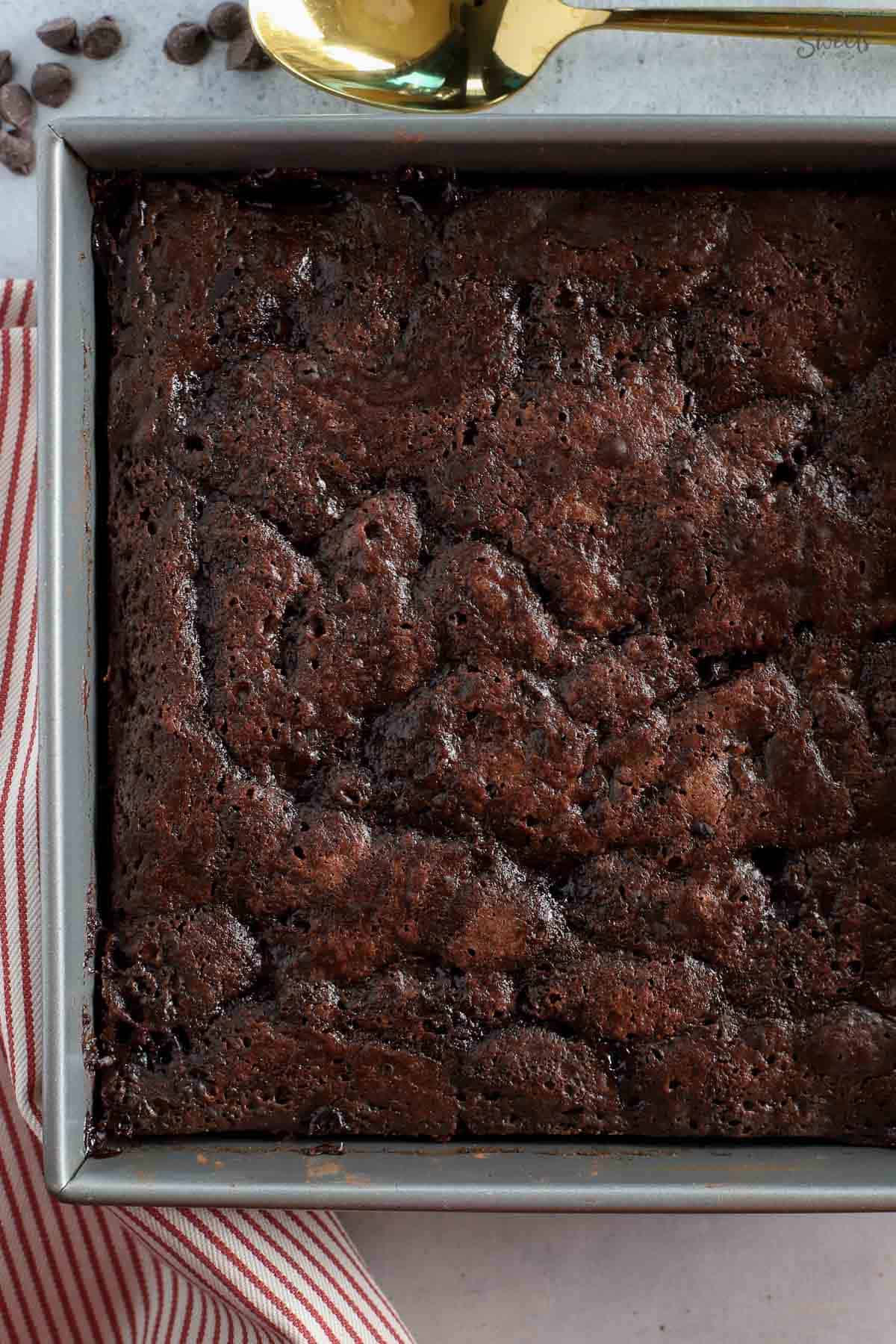 Chocolate pudding cake in a metal cake pan next to a red and white napkin.