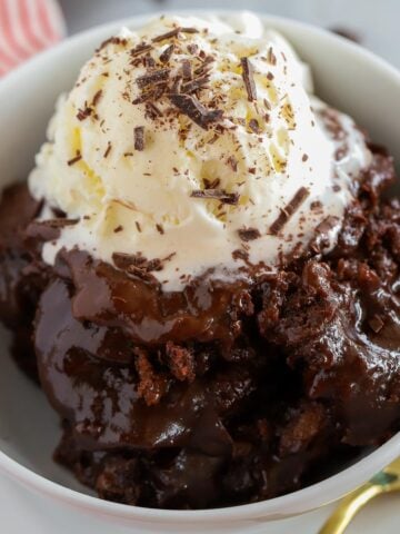 Chocolate pudding cake in a white bowl topped with vanilla ice cream and chocolate shavings.