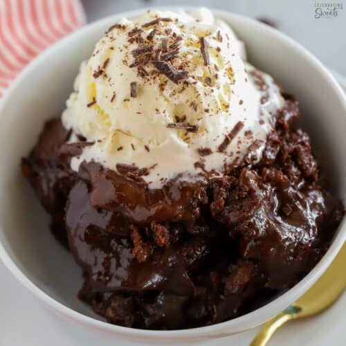Chocolate pudding cake in a white bowl topped with vanilla ice cream and chocolate shavings.
