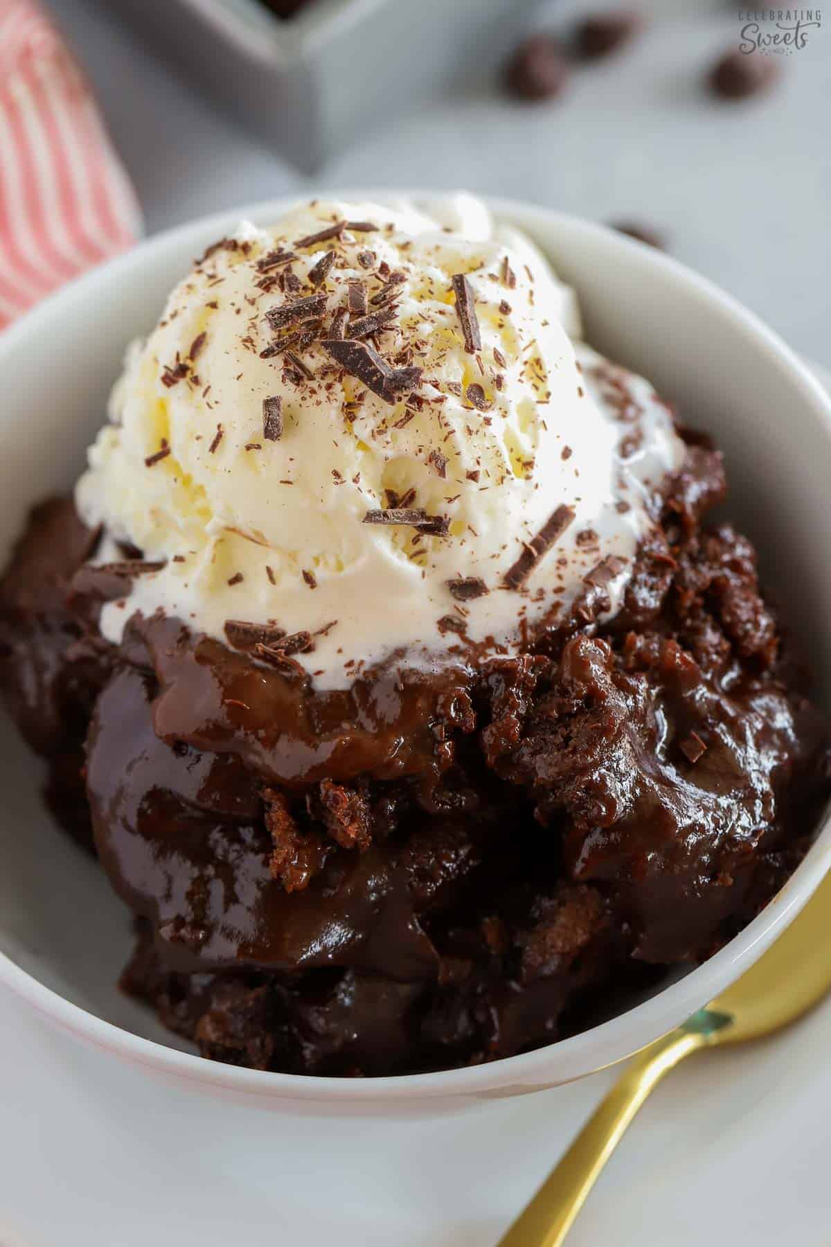 Chocolate pudding cake in a white bowl topped with vanilla ice cream and chocolate shavings.