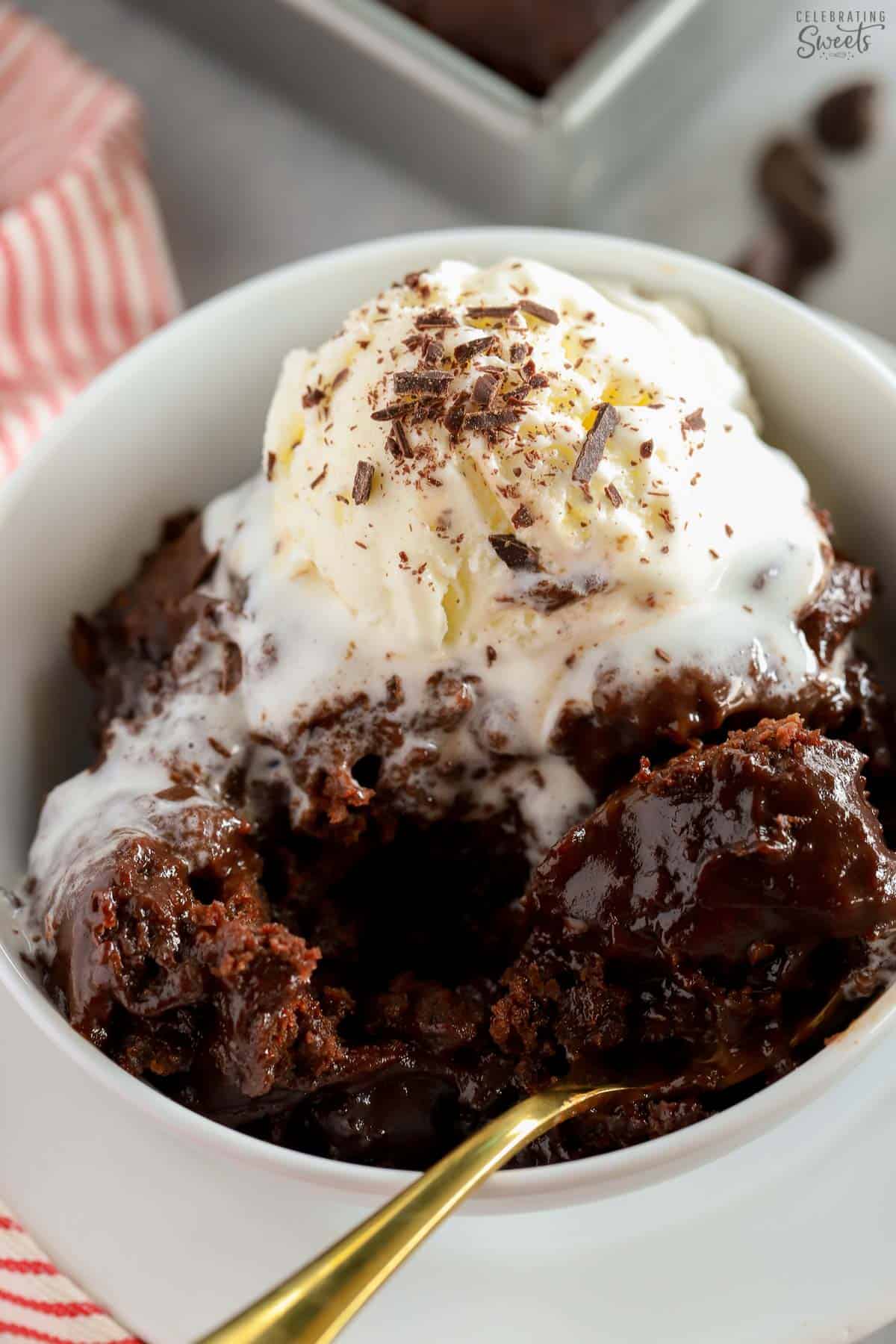 Chocolate pudding cake in a white bowl topped with vanilla ice cream and chocolate shavings.