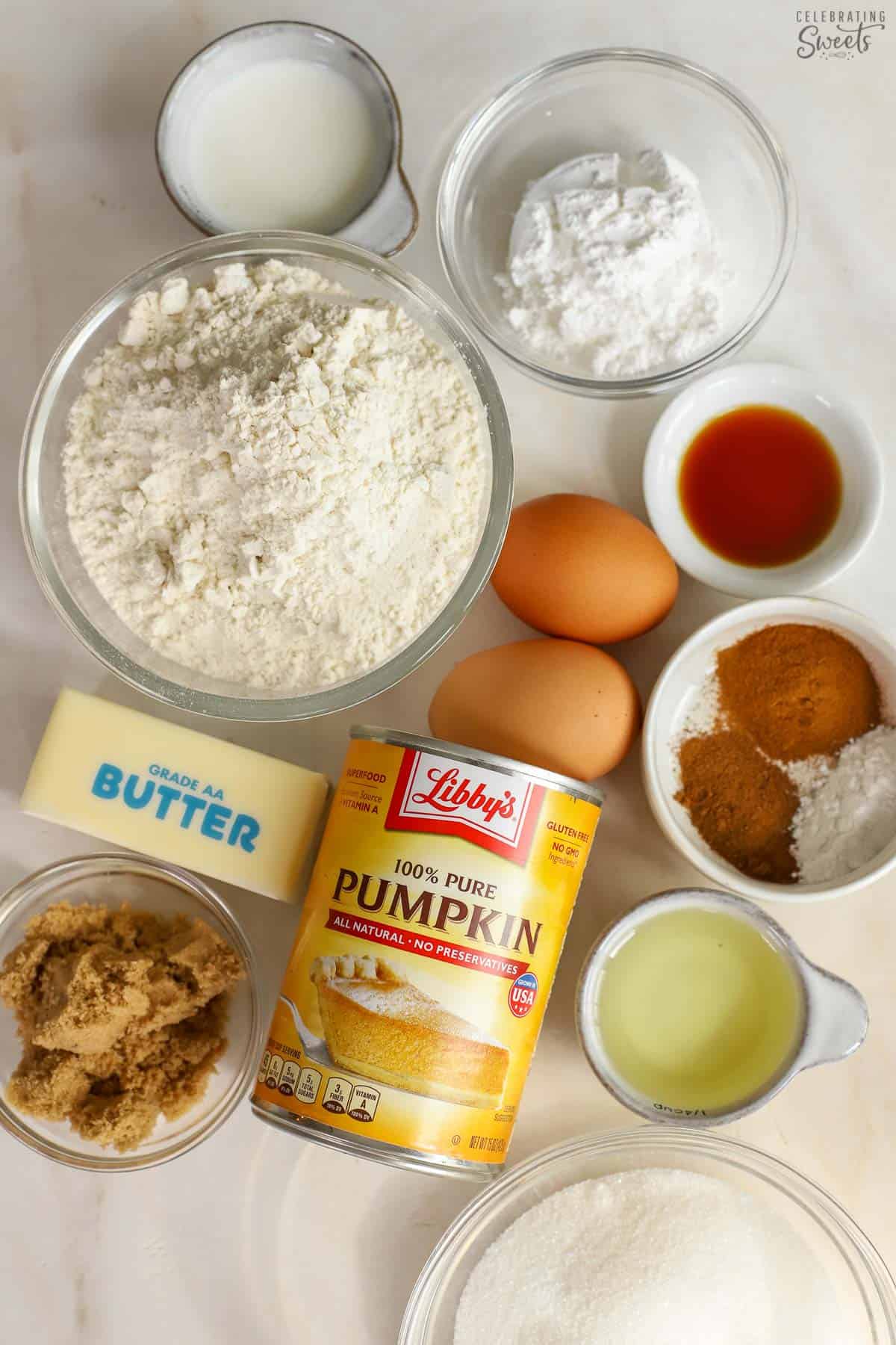 Ingredients to make pumpkin muffins (sugars, flour, canned pumpkin, spices, eggs, butter, oil, milk).
