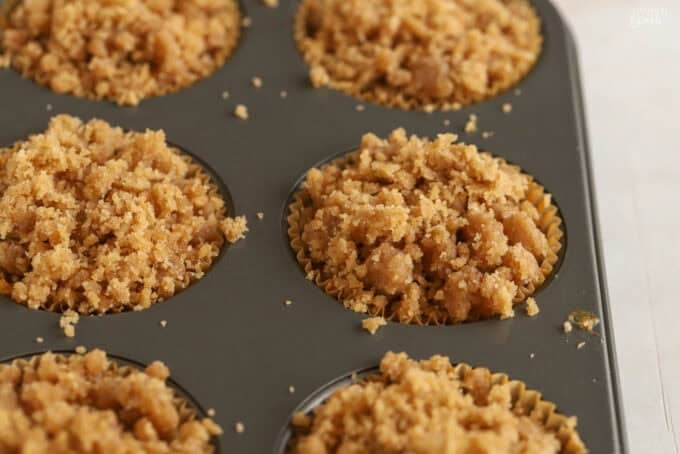 Unbaked pumpkin muffins with crumb topping in a metal muffin pan.