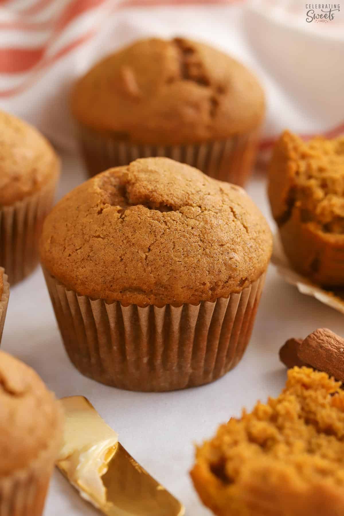 Pumpkin muffins next to a gold knife with butter on it.