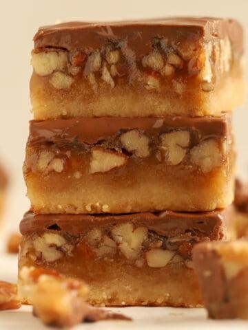 Three chocolate caramel pecan bars stacked on top of each other.