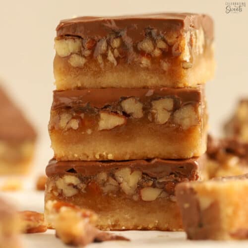 Three chocolate caramel pecan bars stacked on top of each other.