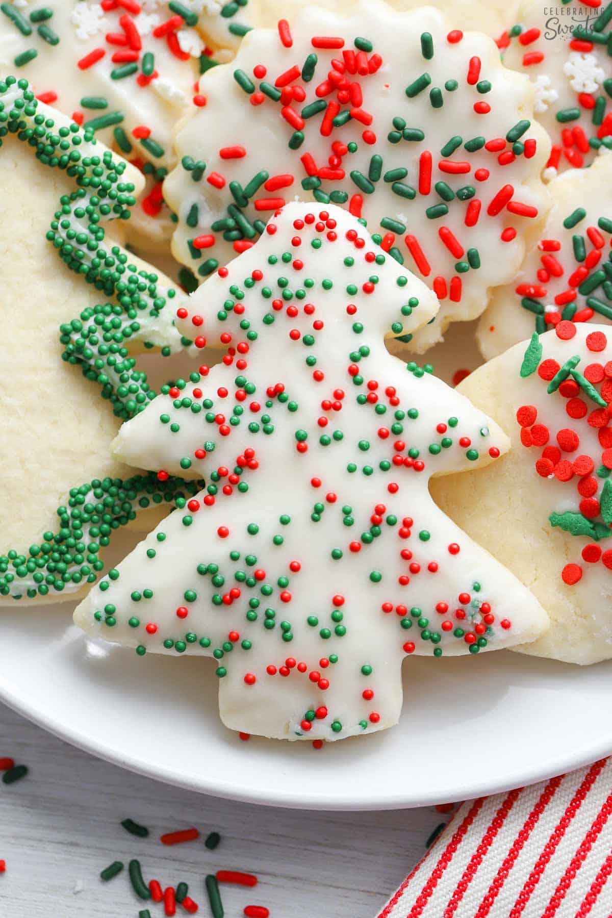 Christmas cutout cookies topped with sugar cookie frosting and red and green sprinkles on a white plate.