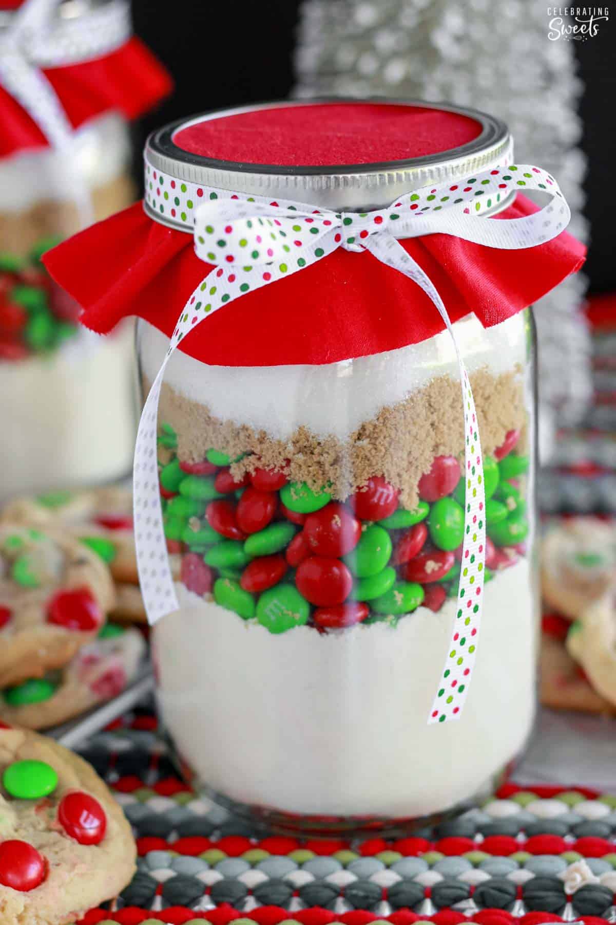 Christmas M&M cookie mix in a jar topped with red fabric and ribbon.