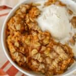 Pumpkin crisp in a white bowl with a scoop of vanilla ice cream.