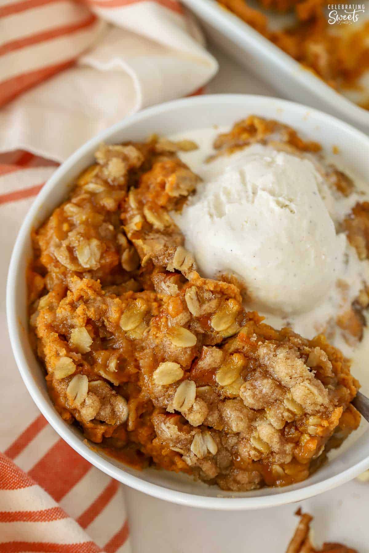Pumpkin crisp in a white bowl topped with vanilla ice cream.
