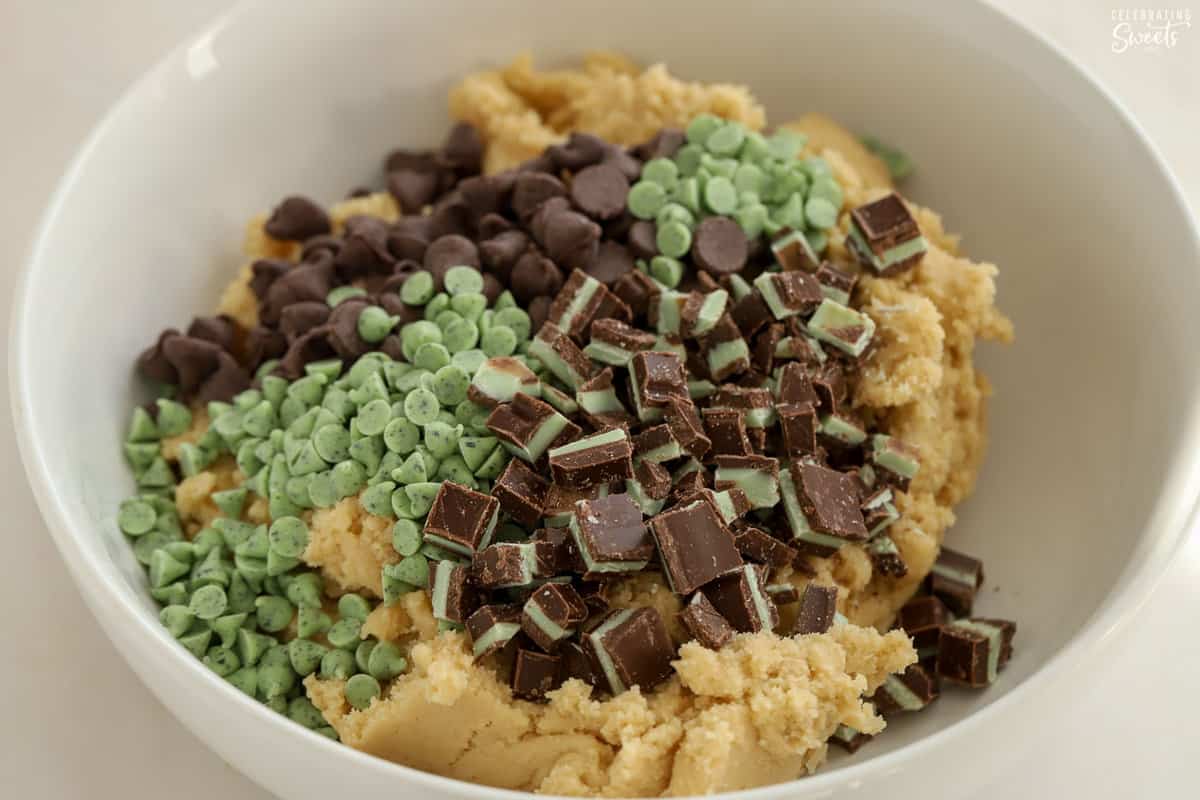 Mint chocolate chip cookie dough filled with mint candy and chocolate chips in a white bowl.