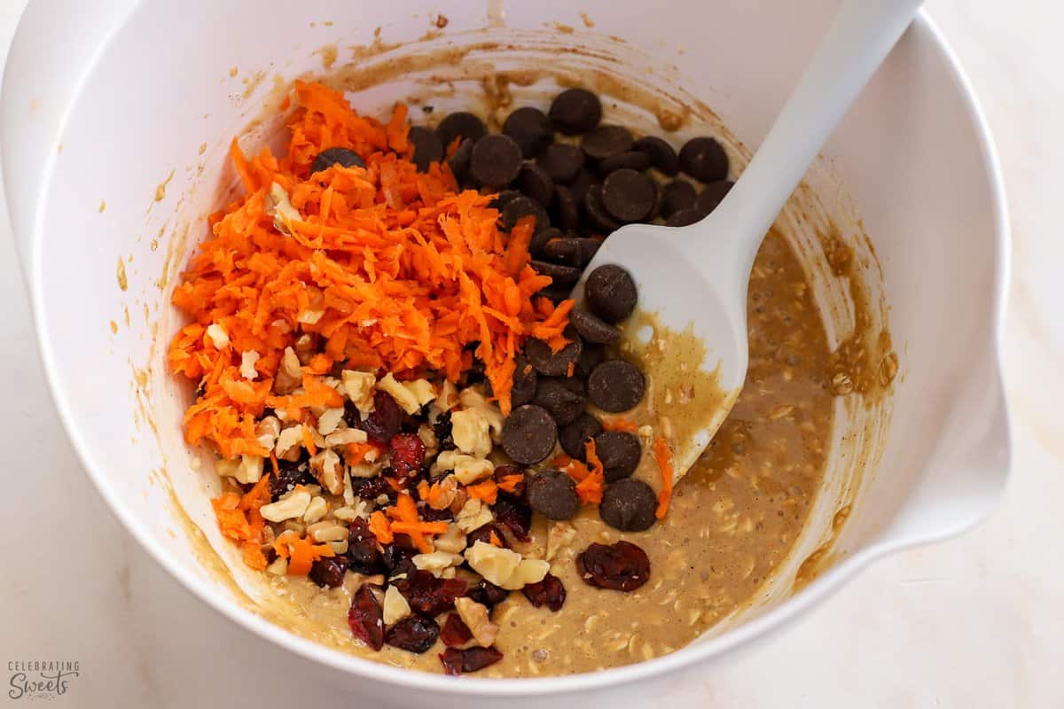 Batter filled with carrots, nuts, dried fruit, and chocolate in a white bowl.