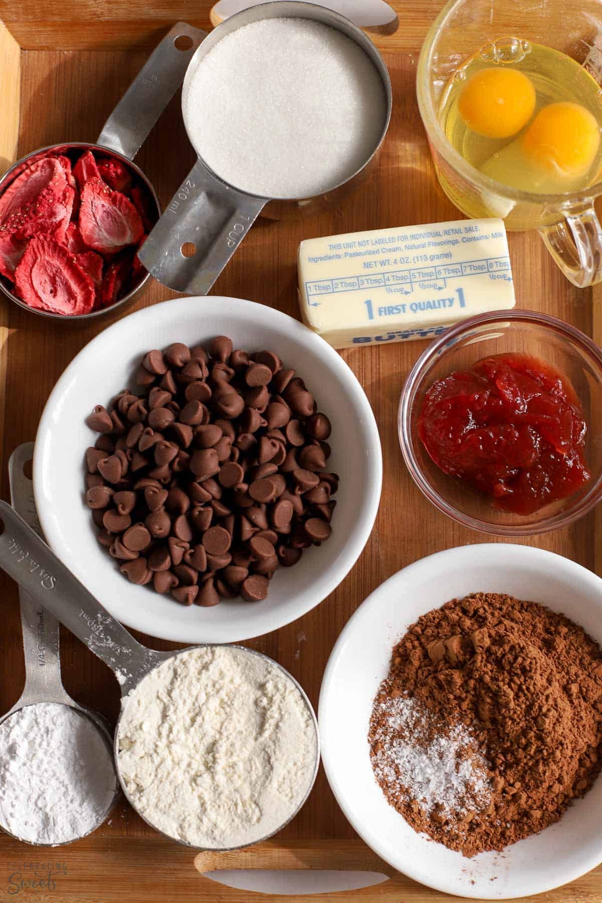 Ingredients to make strawberry brownies: cocoa powder, flour sugar, strawberries, jam, butter, eggs,