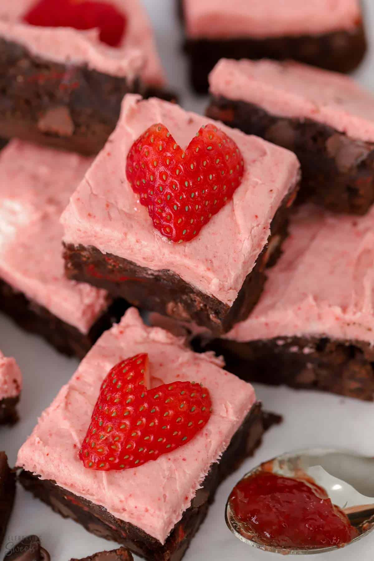 Strawberry brownies on parchment paper topped with heart shaped strawberries.