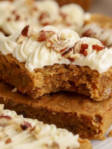 Two carrot cake bars stacked on top of each other with a bite taken out of it.