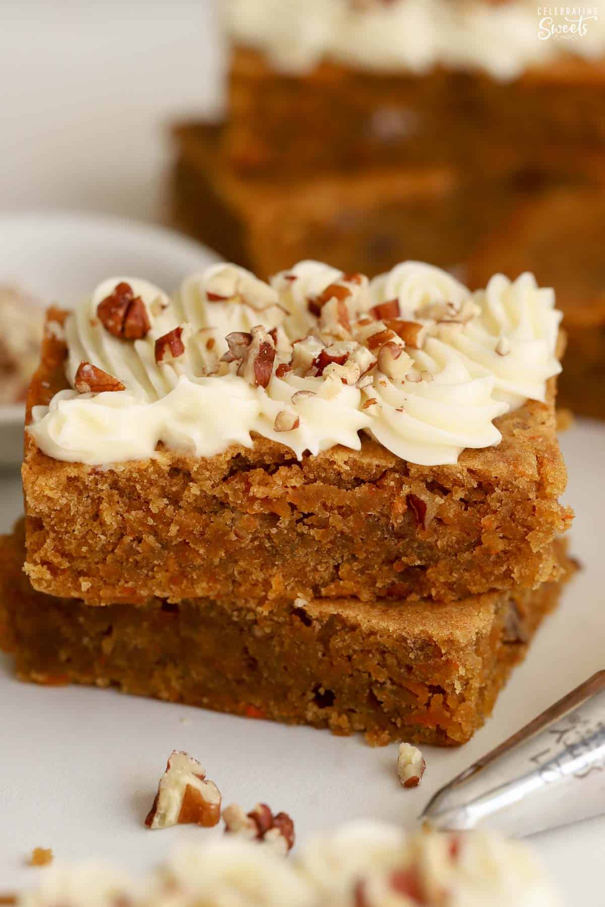 Two carrot cake bars stacked on top of each other topped with frosting and pecans.