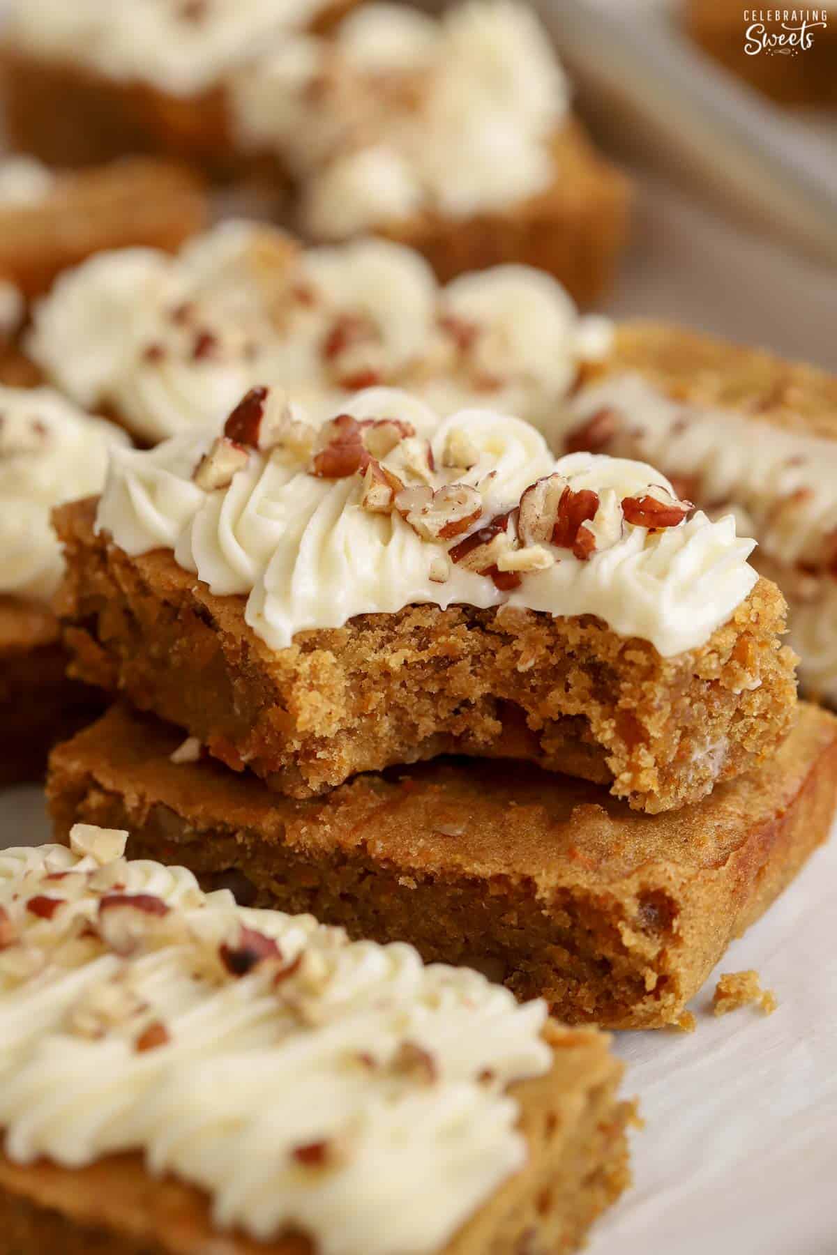Stack of two carrot cake bars topped with cream cheese frosting and pecans.