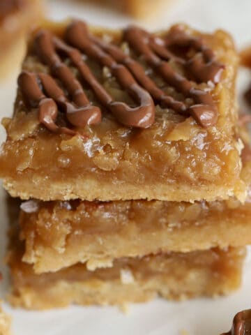 Stack of three caramel coconut bars on parchment paper.