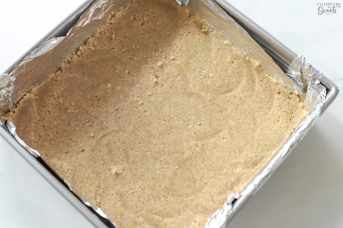 Shortbread cookie crust in a foil-lined square pan.