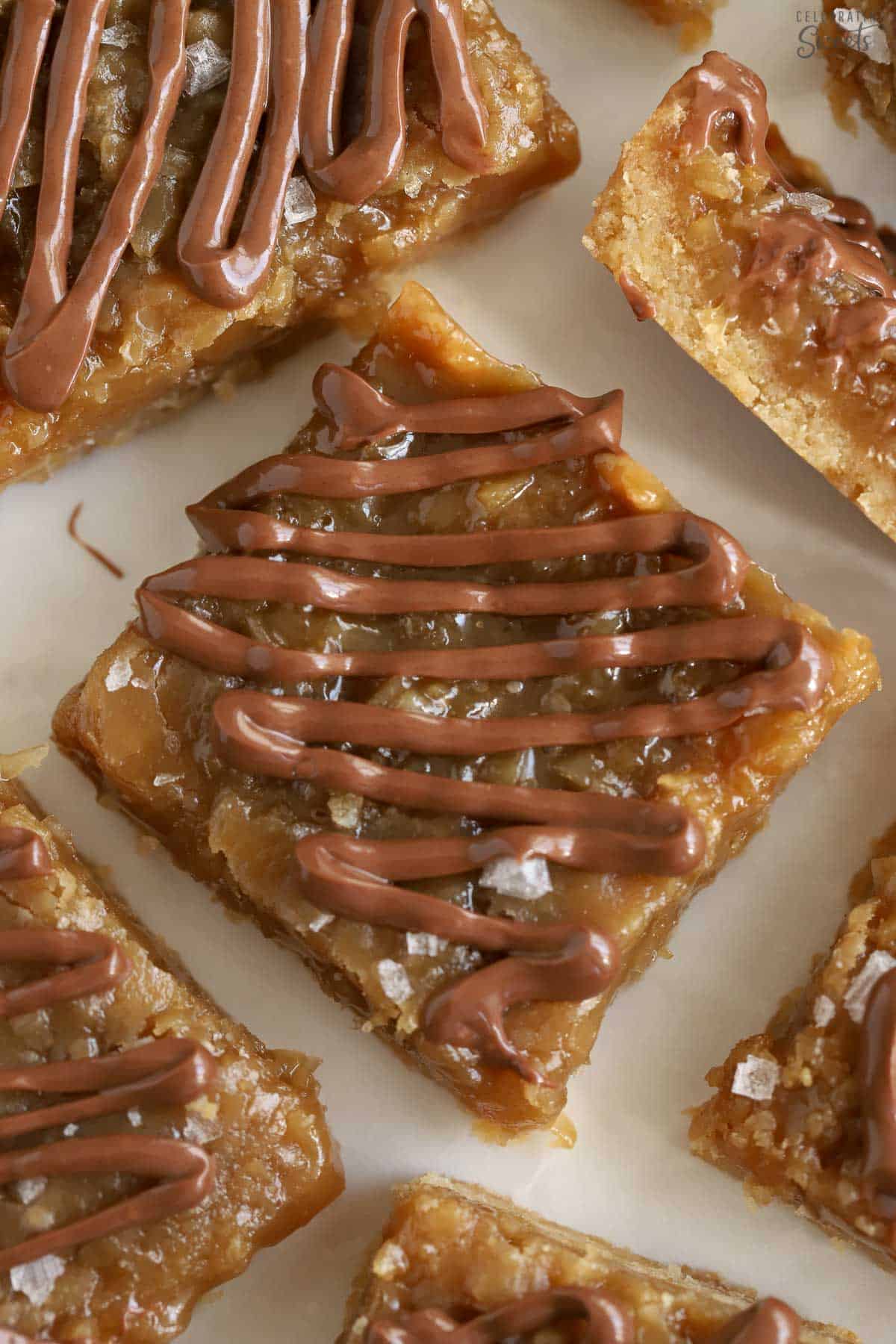 Caramel coconut bars topped with melted chocolate on parchment paper.