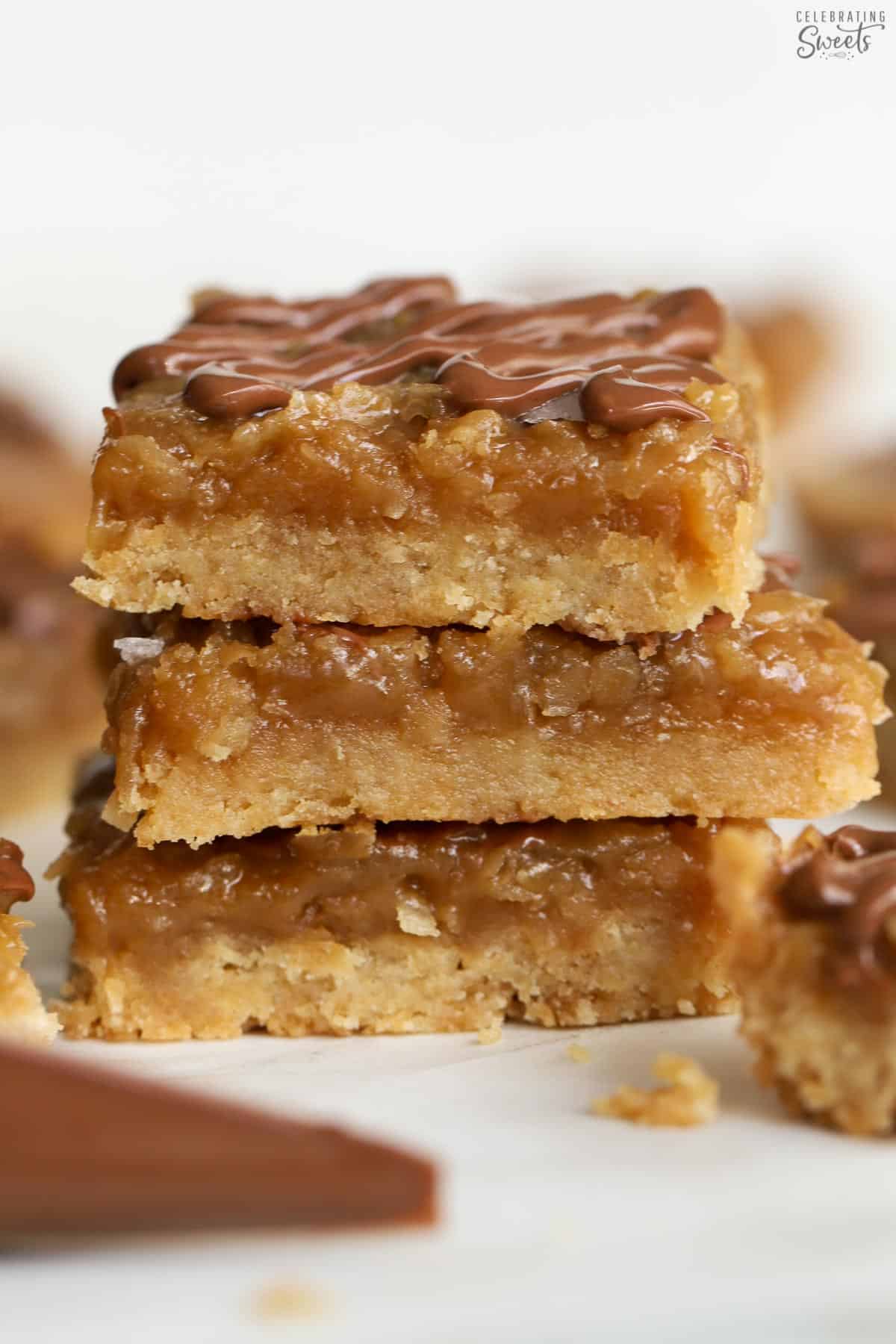 Stack of three caramel coconut bars on parchment paper.