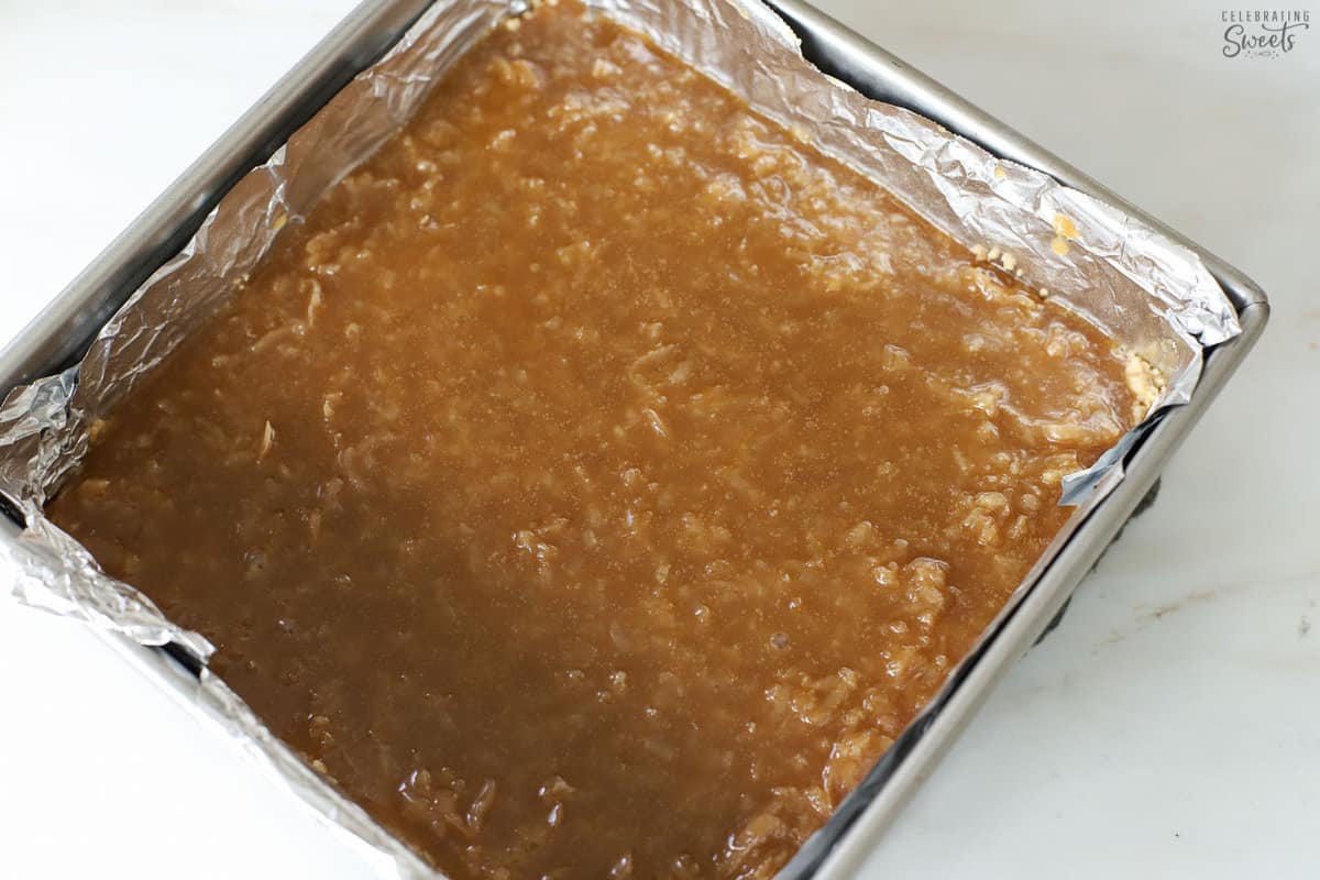 Unbaked coconut bars in a foil-lined square baking dish.