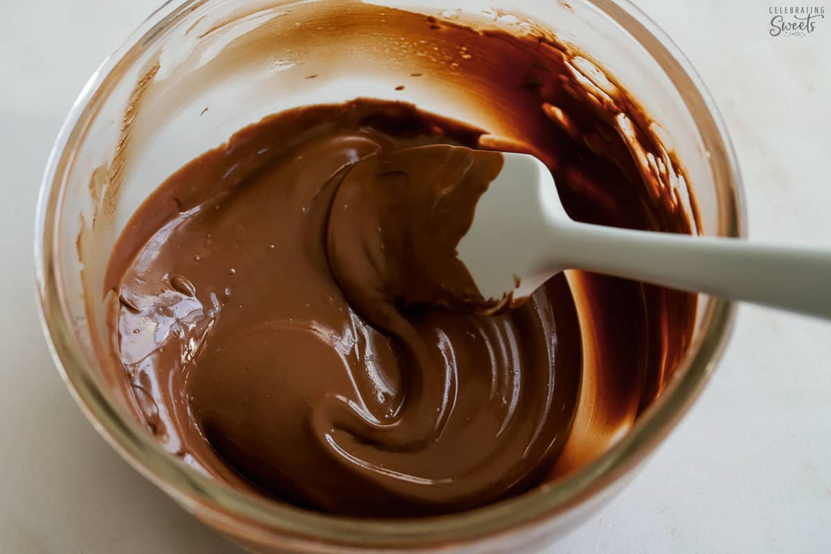Melted chocolate in a glass bowl with a grey spatula.
