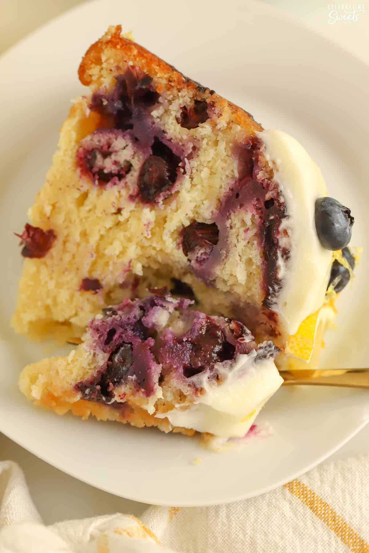 Slice of lemon blueberry bundt cake on a white plate with a gold fork.