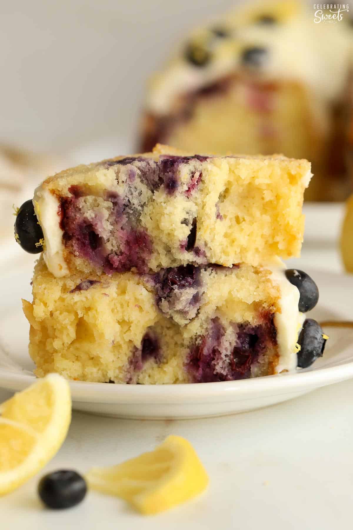 Two pieces of lemon blueberry bundt cake stacked on top of each other on a white plate.
