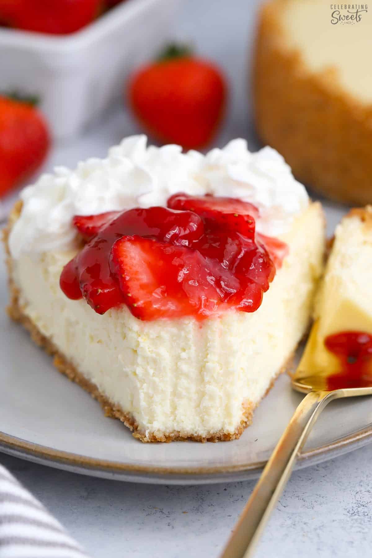 Slice of Greek yogurt cheesecake topped with strawberries and whipped cream on a grey plate.