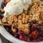 Blueberry peach crisp in a white baking dish topped with ice cream.