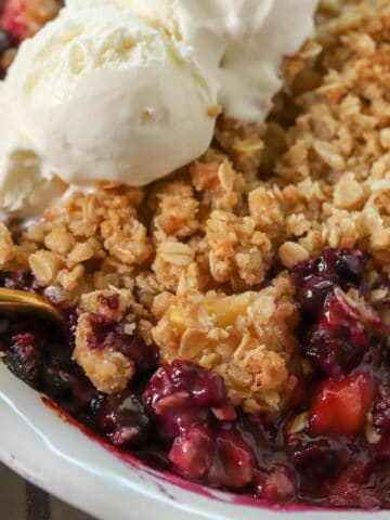 Blueberry peach crisp in a white baking dish topped with ice cream.