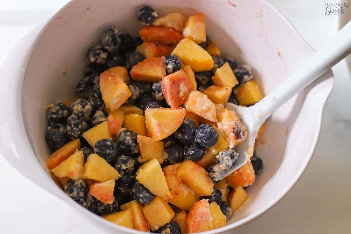 Peaches and blueberries in a white bowl tossed with flour and sugar.