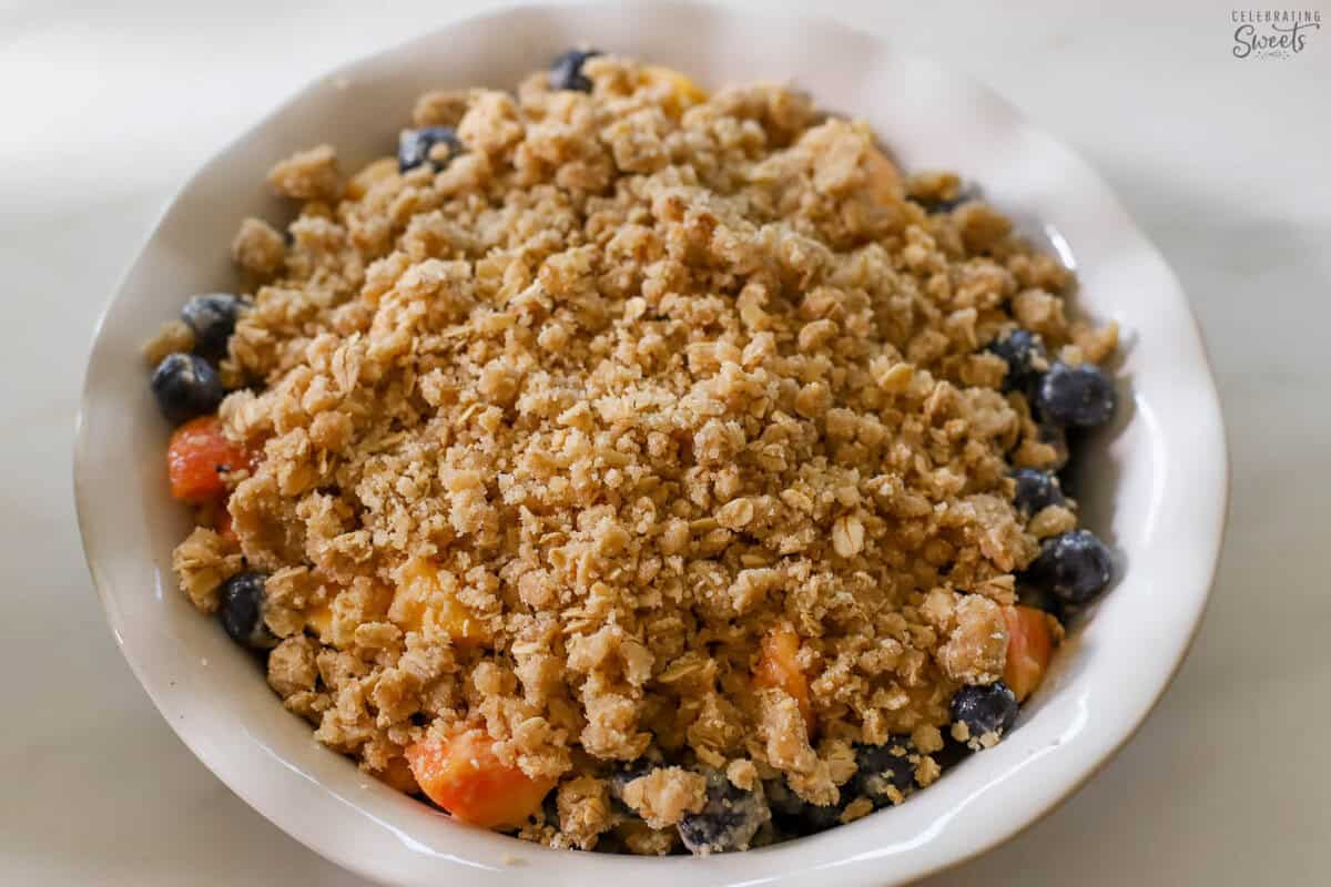 Unbaked blueberry peach crisp in a white baking dish.