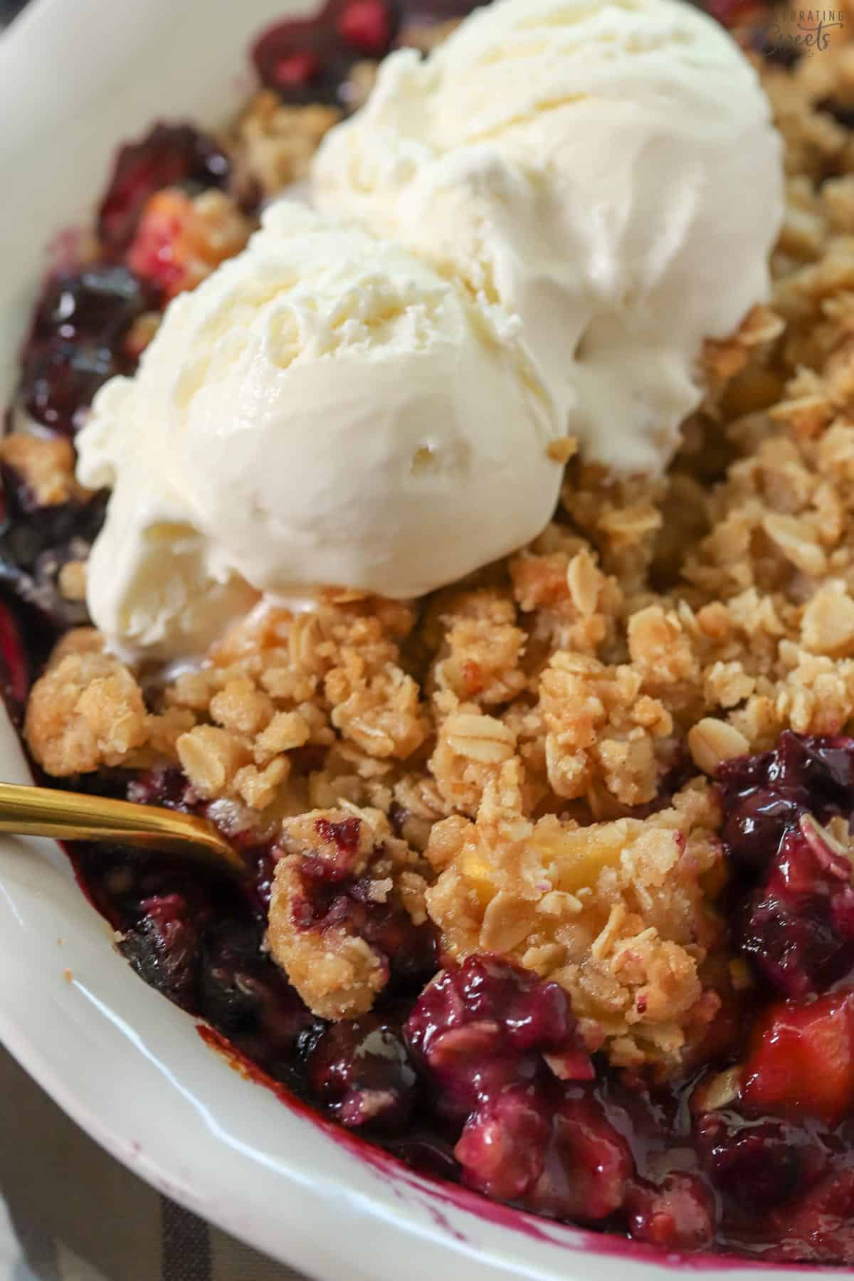 Blueberry peach crisp in white baking dish topped with ice cream.