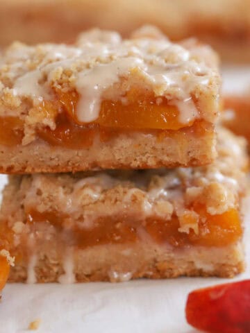 Stack of two peach crumb bars topped with white icing.