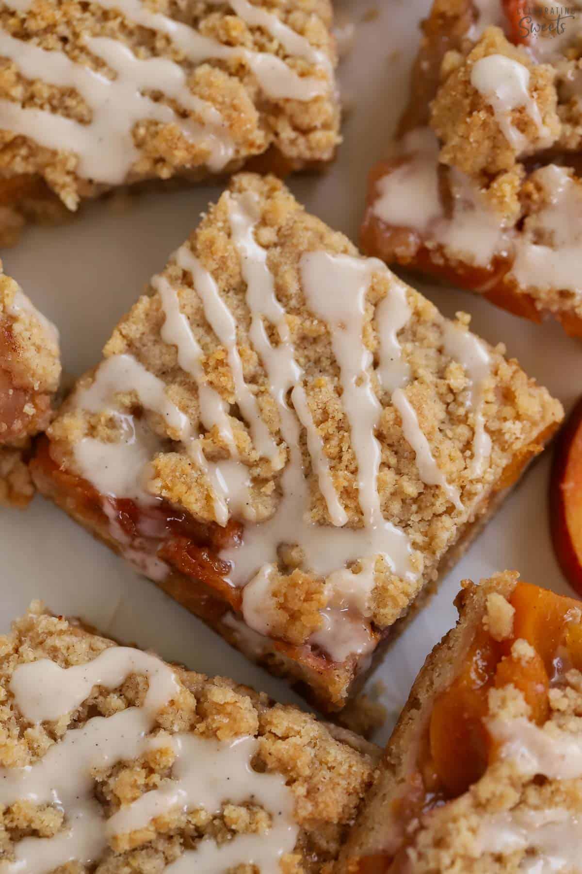 Peach bar topped with crumb topping and white icing on a piece of parchment paper.